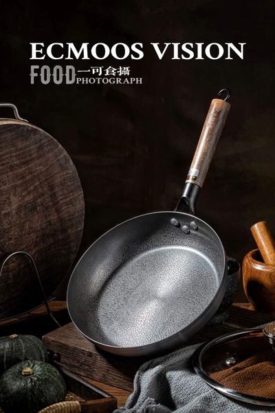 A dark, moody, professional product shot of a high-quality frying pan staged with natural textures and wooden elements.