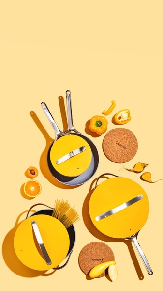 A high-angle flat-lay shot of bright yellow cookware arranged with complementary fresh ingredients, emphasizing color harmony and product design.