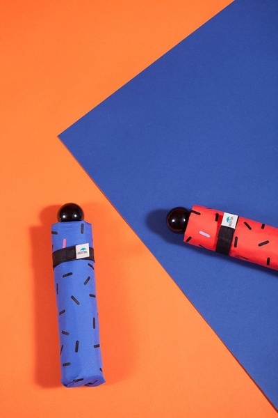 This creative displays two compact umbrellas on a split-screen background of orange and blue to emphasize product portability and color availability.