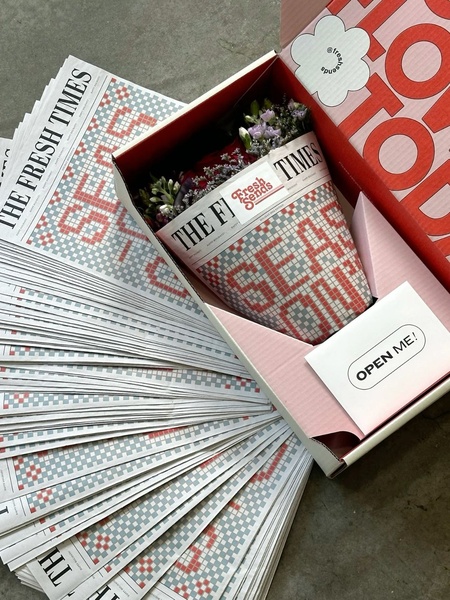 A top-down, aesthetic shot showcasing a fresh bouquet inside branded newspaper wrapping, presented within a clean, minimalist delivery box.