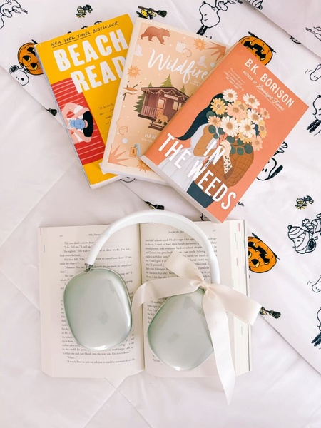 A high-angle flat lay featuring wireless headphones with a decorative ribbon, surrounded by popular romance novels on a themed bedspread.