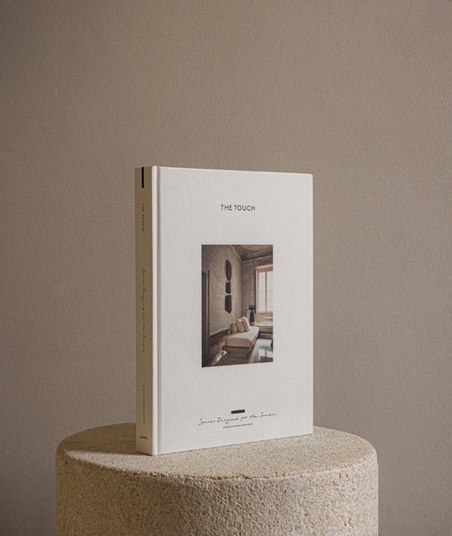 A high-quality studio shot of a coffee table book displayed on a textured stone pedestal against a neutral backdrop.