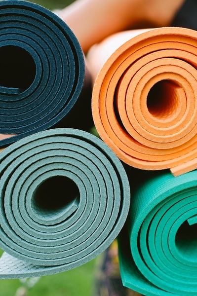 A close-up, high-angle shot of four rolled yoga mats in vibrant teal, navy, orange, and light green, emphasizing the material texture.