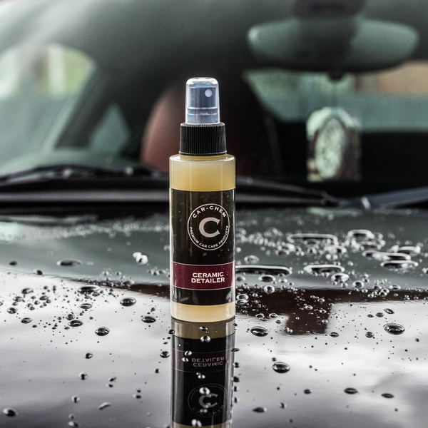 A close-up, high-clarity product shot of a ceramic detailer bottle sitting on a rain-dusted car hood, emphasizing professional quality.