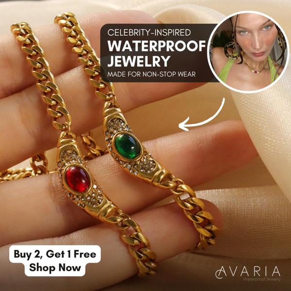 A close-up product shot featuring two gold chain necklaces with red and green gemstone pendants held in a hand.