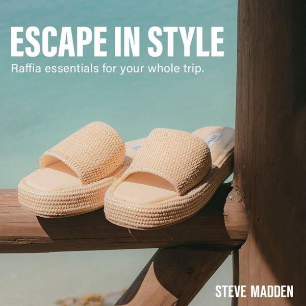 A high-angle shot of neutral-toned raffia slide sandals resting on a wooden railing against a blurred tropical ocean backdrop.