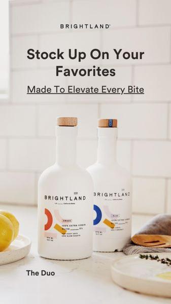 A clean, bright, and aspirational product shot featuring two premium olive oil bottles on a kitchen counter, focusing on brand elegance.
