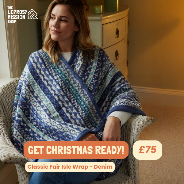A high-quality lifestyle shot featuring a model wrapped in a denim fair isle shawl, highlighting seasonal pricing and comfort.