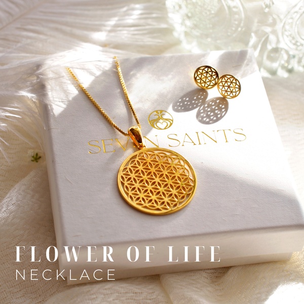 A high-end, minimalist product shot of a gold Flower of Life necklace placed on a white jewelry box with matching stud earrings.