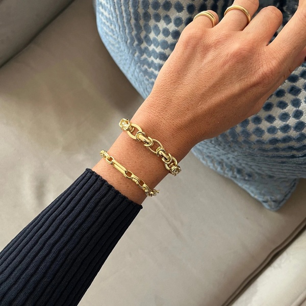 A close-up, natural light shot of a person wearing stacked gold chain bracelets against a soft blue textured cushion.