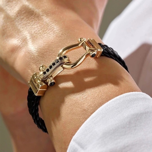 A close-up, high-detail shot of a gold and black braided bracelet worn on a wrist, emphasizing material texture and luxury hardware.