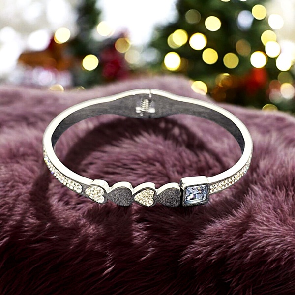A high-contrast, professional product shot of a heart-themed bracelet resting on a plush purple fabric against a bokeh holiday backdrop.