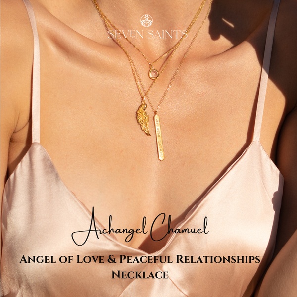 A close-up aesthetic shot of a gold angel wing and bar necklace worn by a person, highlighting the brand and product theme in a warm, sunlight-drenched setting.