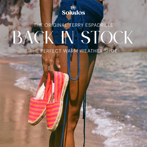 A lifestyle-focused product shot featuring a woman holding a pair of bright striped espadrilles at the beach, emphasizing seasonal availability.