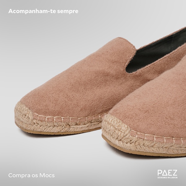A clean, high-angle studio shot of an espadrille loafer set against a soft grey background, emphasizing the textile texture and simple, elegant branding.