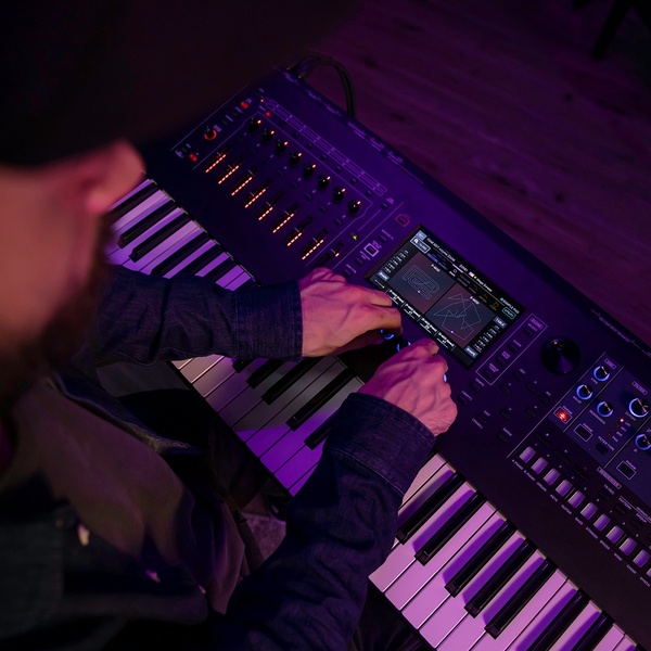 A close-up, high-contrast POV shot of a musician adjusting a professional synthesizer keyboard in a dimly lit studio environment.