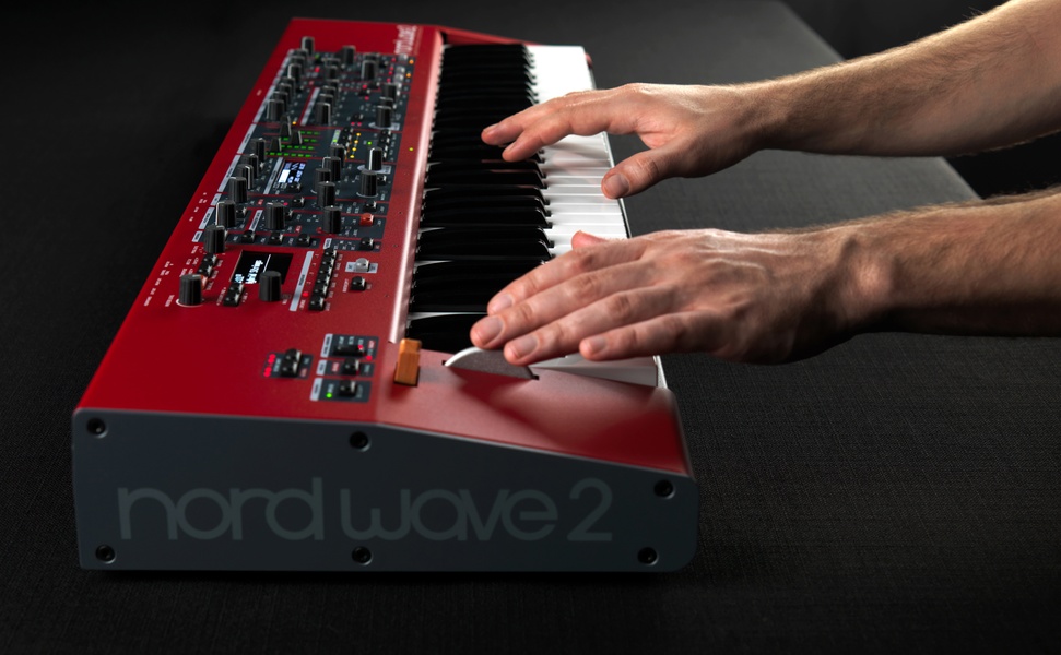 A close-up shot capturing a musician's hands playing a red synthesizer, focusing on the tactile interface and professional performance mood.