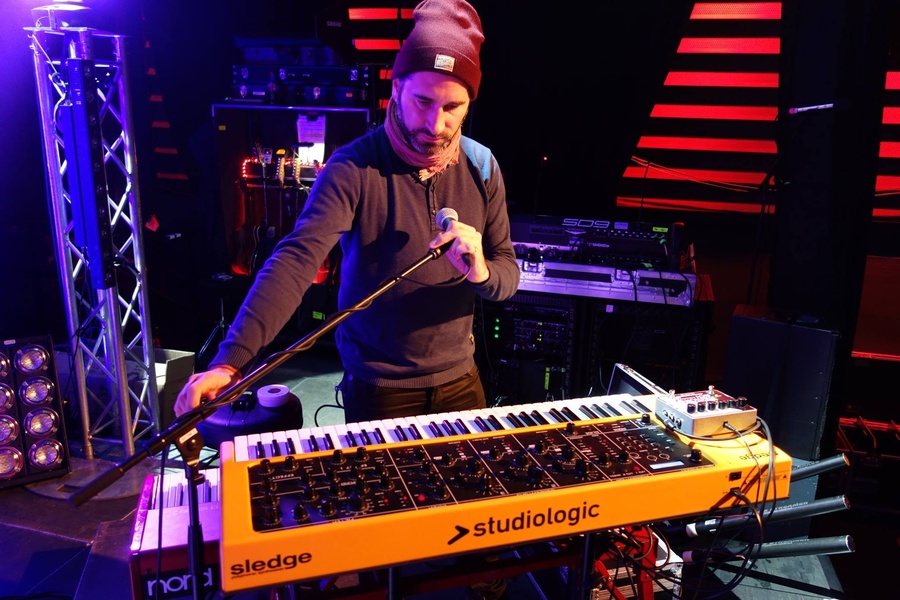 A high-quality, authentic image of a musician performing live while operating a yellow synthesizer keyboard on stage.