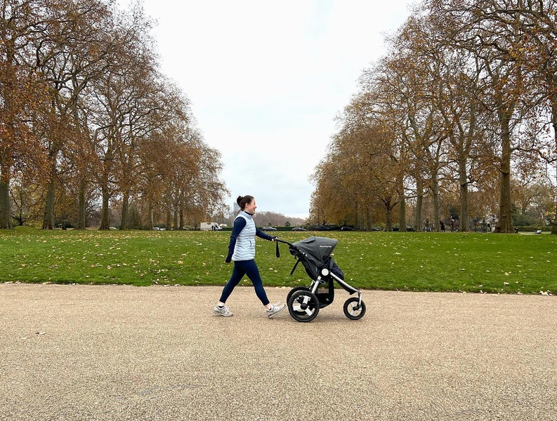 A side-profile shot of a parent using a jogging stroller in a natural outdoor park setting, emphasizing ease of movement.