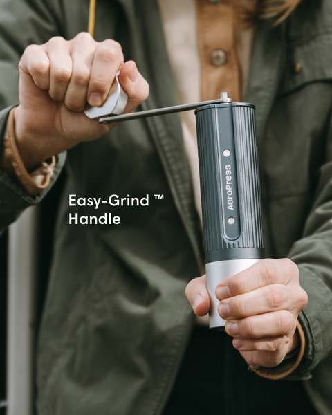 A close-up, high-focus shot of a user operating a manual coffee grinder, emphasizing the physical ease of the grinding handle.