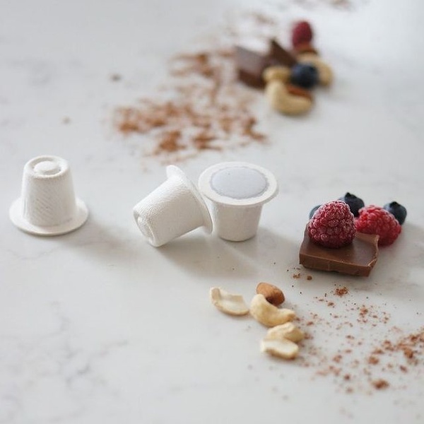 A clean, high-angle studio shot featuring coffee pods surrounded by raw ingredients like chocolate and berries on a marble surface.