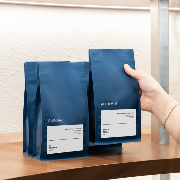 A close-up, high-key shot of a hand placing a bag of premium coffee on a wooden shelf next to other product units.