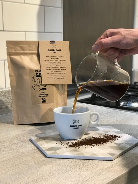 A clean, high-contrast studio shot showing coffee being poured into a branded cup next to a bag of coffee beans, highlighting product quality.