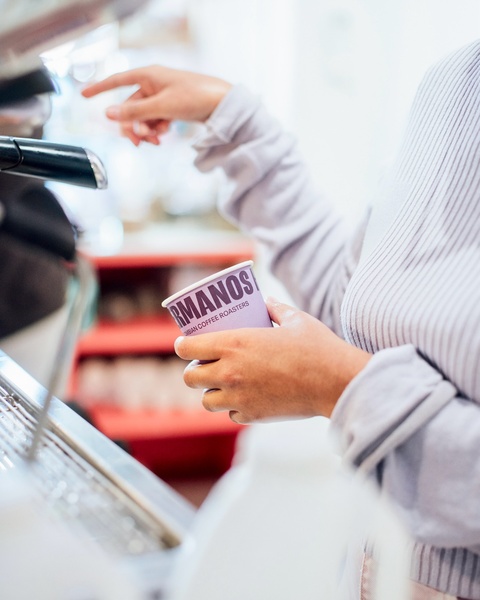 A close-up shot focusing on a branded paper coffee cup being prepared by a barista, highlighting the product in a natural, high-intent setting.