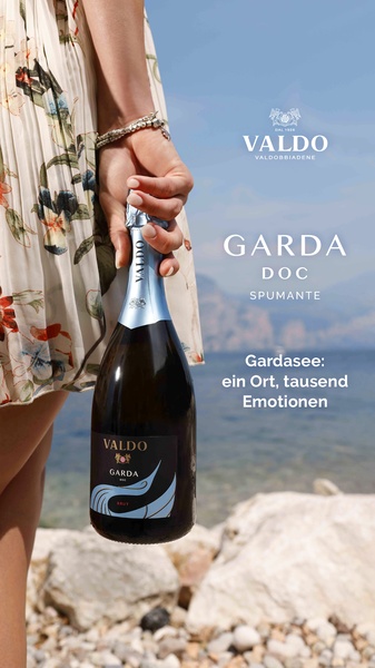 A high-quality lifestyle shot featuring a woman holding a bottle of Spumante by the lake, focusing on branding and atmosphere.
