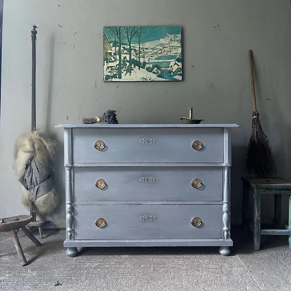 A static 1:1 image showcasing a painted vintage dresser in a neutral, rustic room, focusing on timeless furniture design.