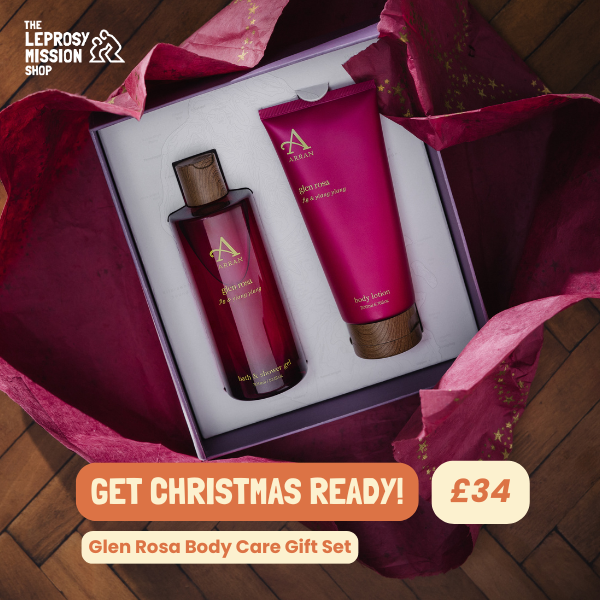 A top-down, elegantly staged product photography shot of a body care gift set inside gift-wrapped packaging, featuring clear price and seasonal call-to-action overlays.