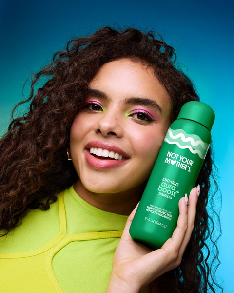 A close-up, high-energy shot of a model holding a branded shampoo bottle against a vibrant, contrasting gradient backdrop.