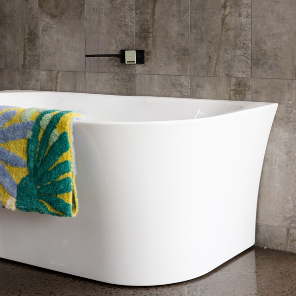 A high-end product hero shot featuring a modern freestanding bathtub accented with a vibrant patterned towel against a textured tile wall.