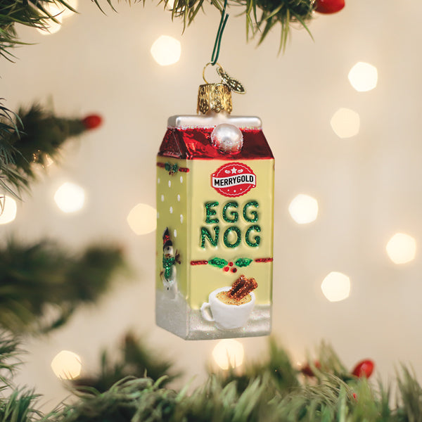 A close-up, high-quality product shot of an eggnog-themed Christmas ornament hanging on a pine tree, surrounded by soft, blurred bokeh lights.