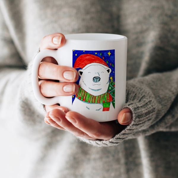 A festive ceramic mug featuring a hand-drawn polar bear wearing a Santa hat, held by a person wearing a cozy sweater to emphasize seasonal warmth.