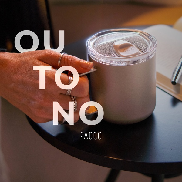 A close-up photograph of a hand holding an insulated mug in a cozy, professional desk setting, using a warm lifestyle aesthetic.