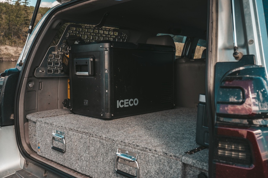 A high-contrast, lifestyle-focused shot of a black portable fridge installed inside the cargo area of an adventure-ready vehicle.