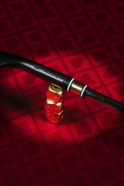 A close-up, high-contrast shot of a Z-Alloy golf club shaft resting on golden dice against a textured red background.