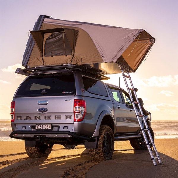 A high-quality, aspirational shot of a vehicle-mounted rooftop tent deployed on a sandy beach during sunset, emphasizing lifestyle appeal.