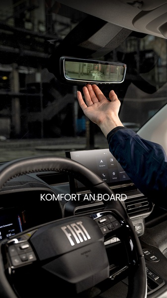 A close-up POV shot from the driver seat of a Fiat, highlighting the advanced rearview mirror system with a hand reaching out to demonstrate interaction.