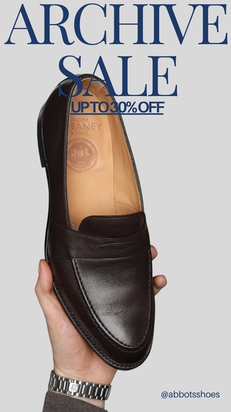 A high-resolution product shot of a leather penny loafer held by a hand, emphasizing texture and luxury craftsmanship with minimal, clear sale messaging.