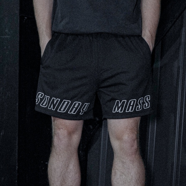 A close-up, dimly lit shot of a person wearing black shorts with white branding, focusing entirely on product placement and aesthetic branding.