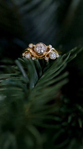 A close-up, high-detail macro shot of a gold diamond ring resting on natural pine needles, creating a luxury festive mood.