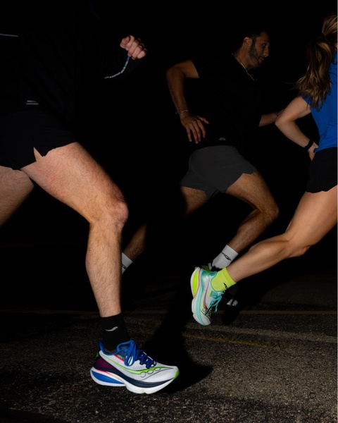 A high-contrast, low-light photograph capturing three runners in motion at night, highlighting the sleek design of the running shoes.