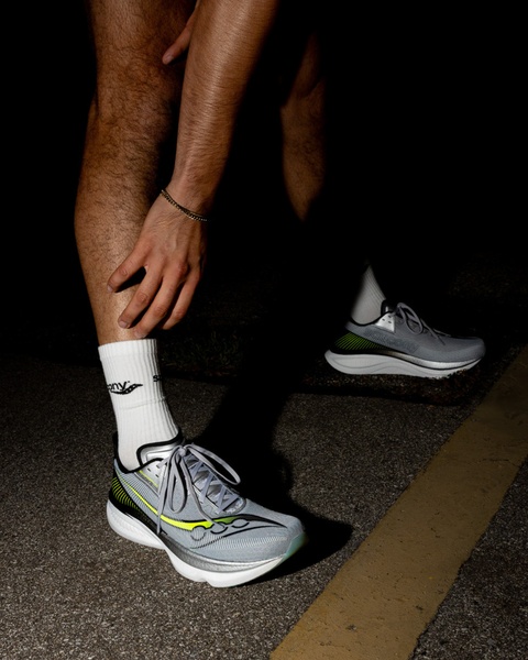 A dark, moody close-up of a runner adjusting their footwear, highlighting the reflective elements of the running shoe against a night-time asphalt background.