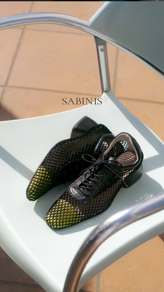 A high-contrast, sun-drenched product shot of mesh flat shoes placed on a light-colored chair.