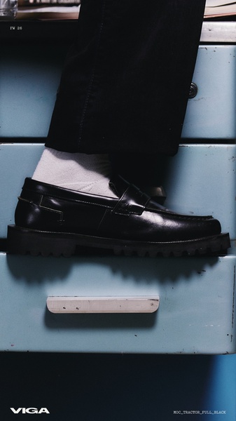 A close-up, high-contrast hero image focusing on a single black loafer positioned on an industrial office drawer unit.