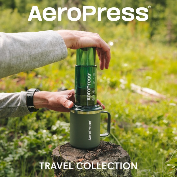 A close-up 1:1 image featuring a hand using an AeroPress coffee maker in a forest setting, emphasizing portable brewing convenience.