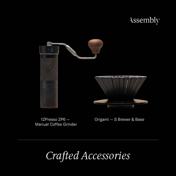 A high-contrast, professional product shot of a manual coffee grinder and an origami dripper set against a solid black background.
