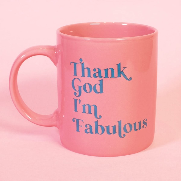 A centered, eye-level shot of a pink ceramic mug featuring bold, blue serif typography on a matching pink background.